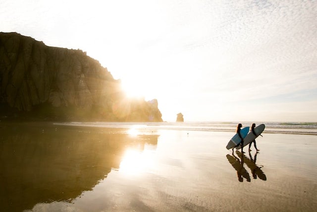 Image of two people carrying surfboards